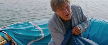 Movie still from “All Is Lost” (2013), directed by J.C. Chandor – An older man is laying on a boat in the water; Medium shot, High angle