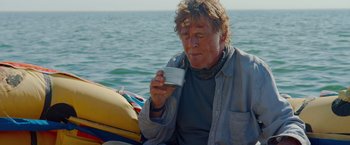 Movie still from “All Is Lost” (2013), directed by J.C. Chandor – An older man sitting on a boat drinking from a cup; Medium shot, Over the shoulder angle