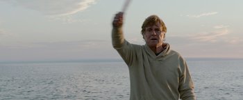 Movie still from “All Is Lost” (2013), directed by J.C. Chandor – An older man holding a frisbee on the beach; Medium shot, Low angle