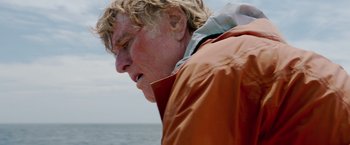 Movie still from “All Is Lost” (2013), directed by J.C. Chandor – A person wearing an orange jacket near the ocean; Close Up shot, Low angle