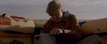 Movie still from “All Is Lost” (2013), directed by J.C. Chandor – A man sitting in a boat writing on a piece of paper; Medium shot, Low angle