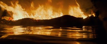 Movie still from “All Is Lost” (2013), directed by J.C. Chandor – A fire is burning in the sky over a body of water; Medium shot, High angle
