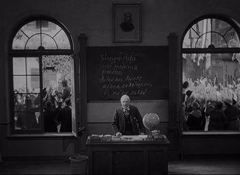 Movie still from “All Quiet on the Western Front” (1930), directed by Lewis Milestone – A man sitting at a desk in front of a chalkboard; Wide shot, High angle