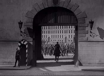 Movie still from “All Quiet on the Western Front” (1930), directed by Lewis Milestone – A black and white photo of a group of people walking through an archway; Extreme Wide shot, High angle