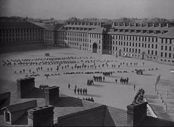 Movie still from “All Quiet on the Western Front” (1930), directed by Lewis Milestone – A black and white photo of a large group of people in a courtyard; Extreme Wide shot, High angle