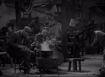 Movie still from “All Quiet on the Western Front” (1930), directed by Lewis Milestone – A group of men sitting around a pot on a stove; Wide shot, High angle
