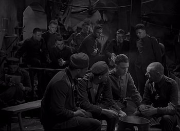 Movie still from “All Quiet on the Western Front” (1930), directed by Lewis Milestone – A black and white photo of a group of men sitting around; Wide shot, High angle