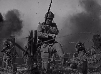 Movie still from “All Quiet on the Western Front” (1930), directed by Lewis Milestone – An old photo of a man holding a rifle in front of barbed wire; Medium shot, Low angle