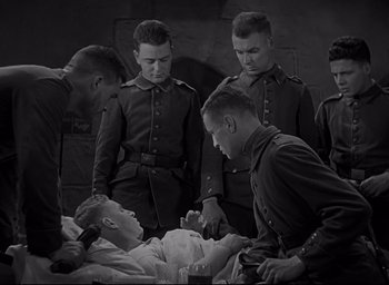 Movie still from “All Quiet on the Western Front” (1930), directed by Lewis Milestone – A black and white photo of a group of men standing around a man in a hospital bed; Medium shot, High angle