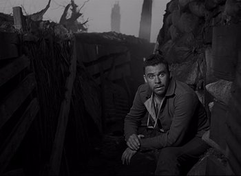 Movie still from “All Quiet on the Western Front” (1930), directed by Lewis Milestone – A black and white photo of a man sitting on a wall; Medium shot, Low angle