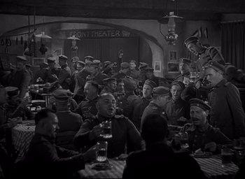 Movie still from “All Quiet on the Western Front” (1930), directed by Lewis Milestone – A group of men sitting at a table in front of a building; Wide shot, High angle