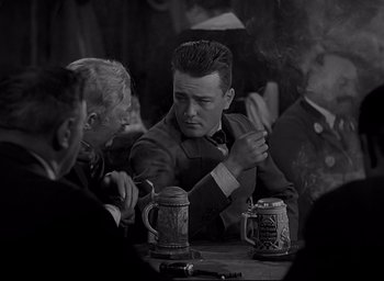 Movie still from “All Quiet on the Western Front” (1930), directed by Lewis Milestone – A man sitting at a table smoking a cigarette; Medium shot, Over the shoulder angle