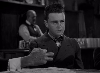 Movie still from “All Quiet on the Western Front” (1930), directed by Lewis Milestone – A man in a suit and tie sitting in front of a bar; Medium shot, Over the shoulder angle