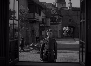 Movie still from “All Quiet on the Western Front” (1930), directed by Lewis Milestone – A man in uniform standing in front of a building; Wide shot, Low angle