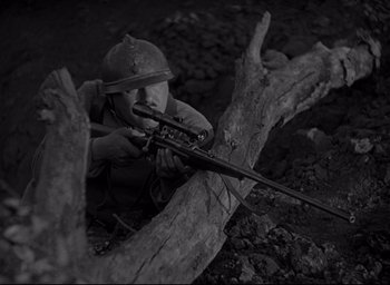 Movie still from “All Quiet on the Western Front” (1930), directed by Lewis Milestone – A man is holding a rifle while sitting on a tree branch; Medium shot, High angle