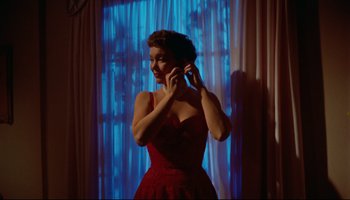 Movie still from “All That Heaven Allows” (1955), directed by Douglas Sirk – A woman in a red dress talking on a cell phone; Medium shot, Low angle