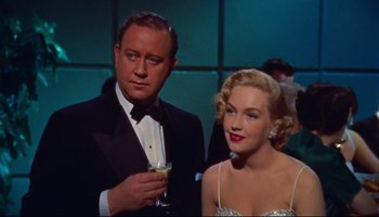 Movie still from “All That Heaven Allows” (1955), directed by Douglas Sirk – A man and a woman standing next to each other holding a drink; Medium shot, Low angle