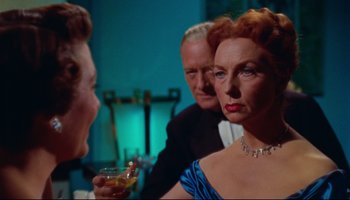 Movie still from “All That Heaven Allows” (1955), directed by Douglas Sirk – An older woman holding a glass in front of two other people; Close Up shot, Over the shoulder angle