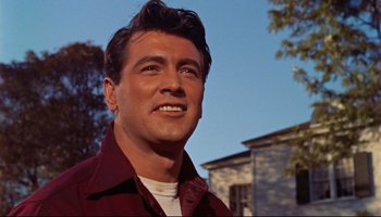 Movie still from “All That Heaven Allows” (1955), directed by Douglas Sirk – A person wearing a red shirt near a building; Close Up shot, Low angle