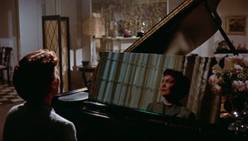 Movie still from “All That Heaven Allows” (1955), directed by Douglas Sirk – A woman sitting at a piano in front of a mirror; Medium shot, Over the shoulder angle