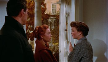 Movie still from “All That Heaven Allows” (1955), directed by Douglas Sirk – Two women and a man standing in front of a house; Medium shot, Over the shoulder angle