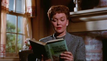 Movie still from “All That Heaven Allows” (1955), directed by Douglas Sirk – A woman reading a book while sitting in a chair; Close Up shot, Low angle