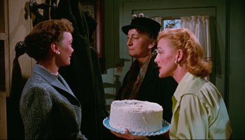Movie still from “All That Heaven Allows” (1955), directed by Douglas Sirk – A group of people standing around a cake; Medium shot, Over the shoulder angle