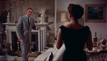 Movie still from “All That Heaven Allows” (1955), directed by Douglas Sirk – A man and a woman are standing in front of a fireplace; Medium shot, Low angle