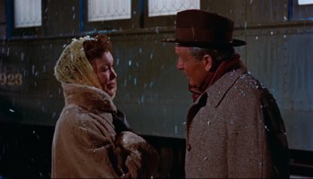 Movie still from “All That Heaven Allows” (1955), directed by Douglas Sirk – An older man and a younger woman standing next to each other in the snow; Medium shot, Low angle