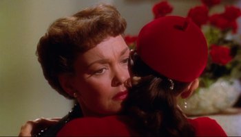 Movie still from “All That Heaven Allows” (1955), directed by Douglas Sirk – An older woman hugging a younger woman in a red hat; Close Up shot, Over the shoulder angle