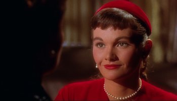 Movie still from “All That Heaven Allows” (1955), directed by Douglas Sirk – A person wearing a red dress and pearls; Close Up shot, Over the shoulder angle
