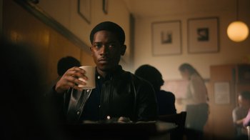 Movie still from “Snowfall” (2017), directed by Hiro Murai – A man sitting at a table holding a coffee mug; Medium shot, Over the shoulder angle