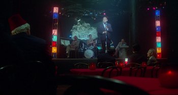 Movie still from “All That Jazz” (1979), directed by Bob Fosse – A man in a suit and tie on stage with a microphone; Wide shot, High angle