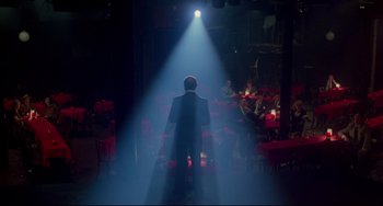 Movie still from “All That Jazz” (1979), directed by Bob Fosse – A man standing on a stage in the middle of a room; Wide shot, High angle