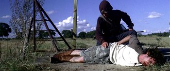 Movie still from “All the Boys Love Mandy Lane” (2006), directed by Jonathan Levine – A man kneeling down on the ground next to a fence; Wide shot, Over the shoulder angle