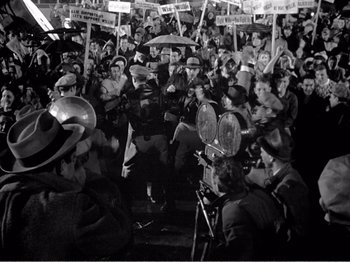 Movie still from “All the King's Men” (1949), directed by Robert Rossen – A group of people holding up signs in front of a crowd of onlookers; Wide shot, High angle