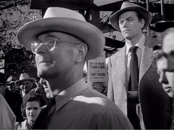 Movie still from “All the King's Men” (1949), directed by Robert Rossen – A man in a hat and a man in a suit and tie standing in front of a crowd; Medium shot, Low angle