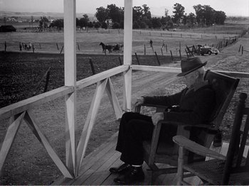 Movie still from “All the King's Men” (1949), directed by Robert Rossen – An older man sitting on a chair on a porch; Wide shot, High angle