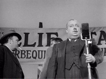Movie still from “All the King's Men” (1949), directed by Robert Rossen – An old photo of a man in a suit holding a selfie stick; Medium shot, Low angle