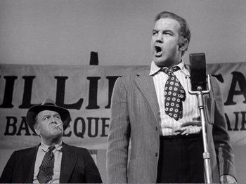 Movie still from “All the King's Men” (1949), directed by Robert Rossen – A man in a suit and tie and a man in a hat and a microphone; Medium shot, Low angle