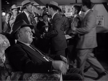Movie still from “All the King's Men” (1949), directed by Robert Rossen – A man in a suit and hat sitting in a crowd; Medium shot, Over the shoulder angle