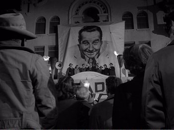 Movie still from “All the King's Men” (1949), directed by Robert Rossen – A group of people gathered around a poster of a man; Medium shot, Low angle