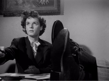 Movie still from “All the King's Men” (1949), directed by Robert Rossen – A woman sitting at a table with her feet on the desk; Medium shot, Low angle