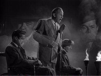 Movie still from “All the King's Men” (1949), directed by Robert Rossen – An old photo of a man speaking on a microphone; Medium shot, Low angle