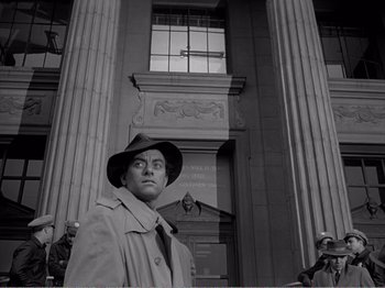 Movie still from “All the King's Men” (1949), directed by Robert Rossen – A man wearing a hat and a trench coat standing in front of a building; Medium shot, Low angle