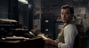 Movie still from “All the King's Men” (2006), directed by Steven Zaillian – A man sitting at a desk holding a book in his hands; Medium shot, Low angle