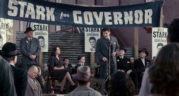 Movie still from “All the King's Men” (2006), directed by Steven Zaillian – A man standing at a microphone in front of a group of people; Medium shot, High angle