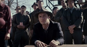 Movie still from “All the King's Men” (2006), directed by Steven Zaillian – A man in a suit and a hat sitting in front of a group of men; Medium shot, Low angle