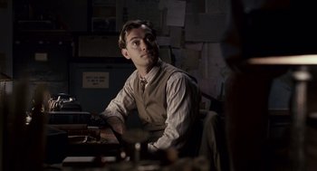 Movie still from “All the King's Men” (2006), directed by Steven Zaillian – A man sitting at a desk in a room; Medium shot, Over the shoulder angle