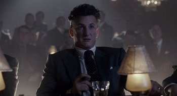 Movie still from “All the King's Men” (2006), directed by Steven Zaillian – A man sitting at a table with a glass in his hand; Medium shot, Low angle